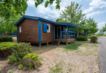 Gemütliche Holzhütte mit blauen Details in einer grünen Umgebung, ideal für ein Glamping-Abenteuer.