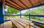 Terraza de madera techada en alojamiento glamping con mesa y bancos, vistas a árboles y colinas verdes.
