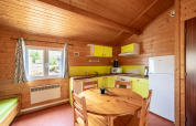 Interno di cucina glamping con pareti in legno, tavolo tondo, frigorifero, finestra e mobili gialli.