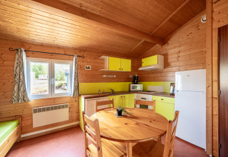Cozy glamping accommodation kitchen with wooden interior, round table, fridge, window and yellow cabinets.