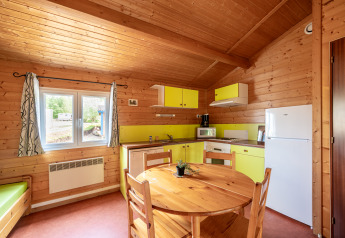 Indvendigt billede af et hyggeligt glampingkøkken med trævægge, spisebord, køleskab og vindue.