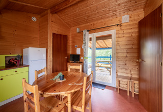 Interior de una acogedora cabaña glamping con paredes de madera, mesa redonda, nevera y terraza exterior.