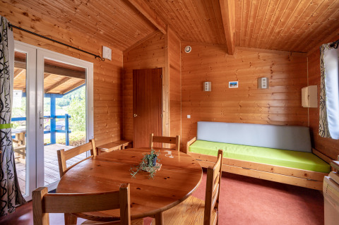 Vista interior de un alojamiento glamping con paredes de madera, mesa redonda y salida a terraza.