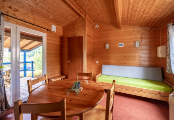 Vista interior de un alojamiento glamping con paredes de madera, mesa redonda y salida a terraza.