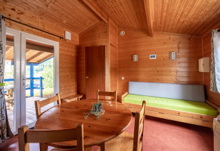 Vista interior de un alojamiento glamping con paredes de madera, mesa redonda y salida a terraza.
