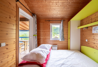 Dormitorio en alojamiento glamping con paneles de madera, cama doble, ventana y vista a la naturaleza.