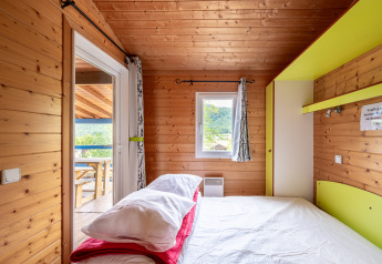 Schlafzimmer in einer Glamping-Unterkunft aus Holz mit Doppelbett, Fenster und Ausblick ins Grüne.