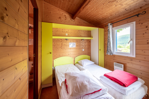 Camera glamping accogliente con due letti singoli, pareti in legno e finestra con vista panoramica.