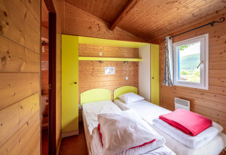 Camera glamping accogliente con due letti singoli, pareti in legno e finestra con vista panoramica.