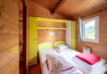 Camera glamping accogliente con due letti singoli, pareti in legno e finestra con vista panoramica.