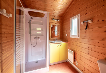 Badezimmer mit Holzverkleidung, Duschkabine, Waschbecken mit Spiegel und Fenster in Glamping-Unterkunft.