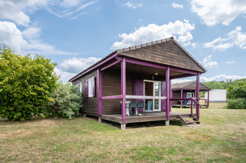 View of Chalet ZEN, a wooden cabin with purple accents, porch, and yard under a partly cloudy sky.