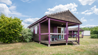 View of Chalet ZEN, a wooden cabin with purple accents, porch, and yard under a partly cloudy sky.