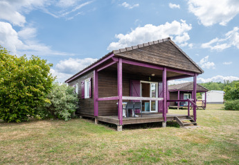 Vista del Chalet ZEN, una cabaña de madera con detalles morados, porche y jardín bajo un cielo parcialmente nublado.
