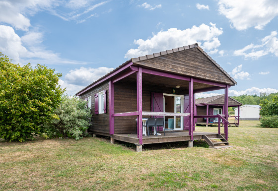 Vista del Chalet ZEN, una cabaña de madera con detalles morados, porche y jardín bajo un cielo parcialmente nublado.