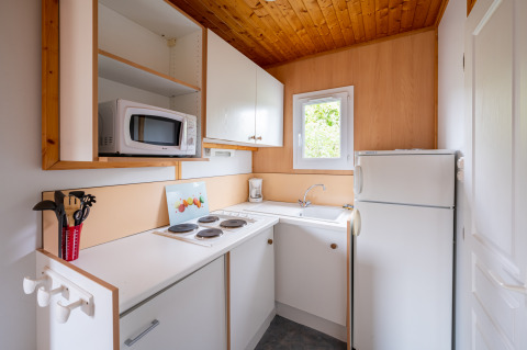 Pequeña cocina en el Chalet ZEN en Camping Seasonova Les Vosges du Nord con nevera, microondas y fregadero.