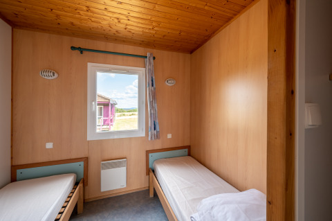 Room with two single beds, wood interior, and a window, Chalet ZEN at Camping Seasonova Les Vosges du Nord, France.