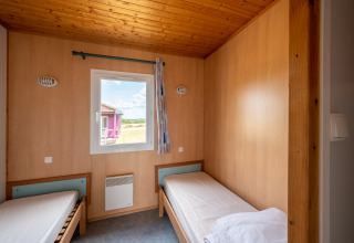 Room with two single beds, wood interior, and a window, Chalet ZEN at Camping Seasonova Les Vosges du Nord, France.