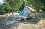 Een foto van een tipi-tent op een houten platform met ligstoelen en tuinset op een groene campinglocatie.
