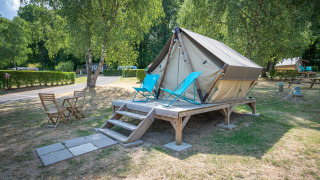 Foto di una tenda tipi su piattaforma di legno con lettini e tavolo da esterno in un campeggio verde.