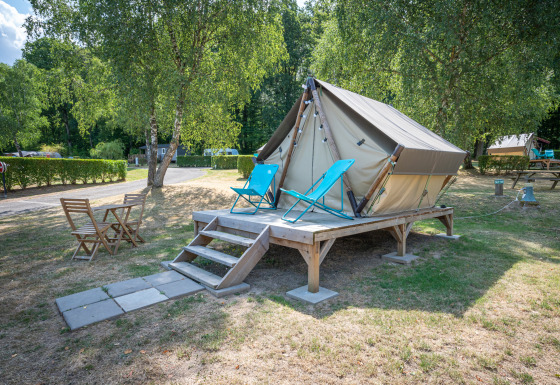 Foto di una tenda tipi su piattaforma di legno con lettini e tavolo da esterno in un campeggio verde.
