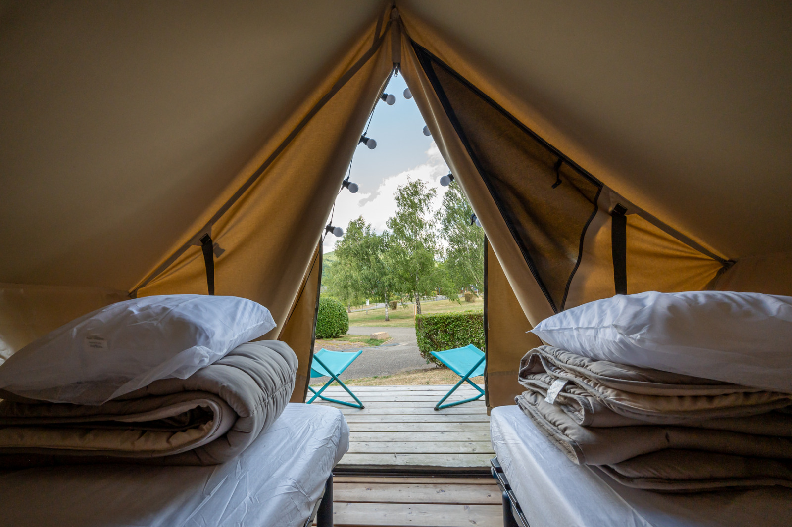 Binnenkant van een tipi-tent met twee bedden, dekens, kussens en uitzicht op terras en natuur.