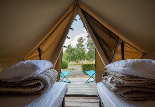 Indersiden af et tipi-telt med to senge, puder, tæpper og udsigt til terrasse og natur udenfor.