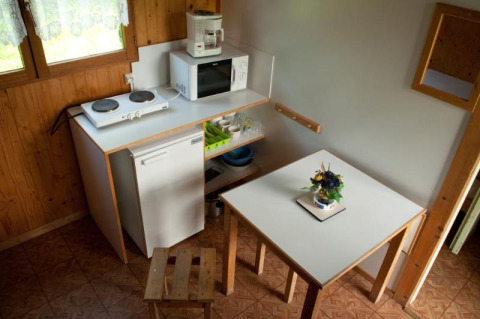 Pequeña cocina en una cabaña con mesa, taburetes, placa eléctrica, nevera, microondas y escurreplatos.