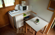Pequeña cocina en una cabaña con mesa, taburetes, placa eléctrica, nevera, microondas y escurreplatos.