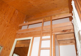 Vista interna di una baita in legno con soppalco e scala a Chalet Olga, Camping Seasonova Les Vosges du Nord.