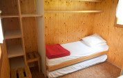 Pequeña habitación de madera con cama individual, estantes y ventana en Chalet Isabelle, Camping Seasonova Les Vosges du Nord.