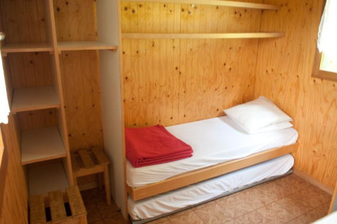 Pequeña habitación de madera con cama individual, estantes y ventana en Chalet Isabelle, Camping Seasonova Les Vosges du Nord.