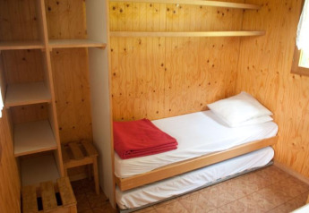 Pequeña habitación de madera con cama individual, estantes y ventana en Chalet Isabelle, Camping Seasonova Les Vosges du Nord.