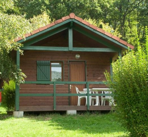 Wooden cabin with front porch and white chairs, surrounded by lush greenery, Chalet Anaïs in nature.