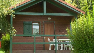 Cabaña de madera con porche y sillas blancas, rodeada de vegetación en Chalet Anaïs en la naturaleza.