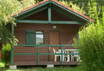 Wooden cabin with front porch and white chairs, surrounded by lush greenery, Chalet Anaïs in nature.