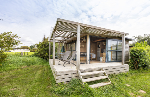 Chalet Evasion Vista met overdekt houten terras, ligstoelen en groene, natuurlijke omgeving buiten.