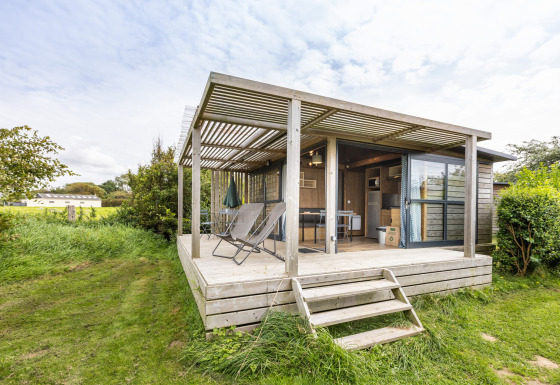 Chalet Evasion Vista met overdekt houten terras, ligstoelen en groene, natuurlijke omgeving buiten.