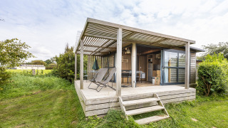 Chalet Evasion Vista met overdekt houten terras, ligstoelen en groene, natuurlijke omgeving buiten.
