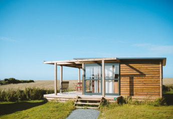 Chalet Evasion Vista bij Huttopia Les Falaises - Normandië, Frankrijk, houten chalet in groene omgeving.