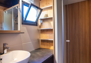 Baño moderno en Chalet Evasion Vista con lavabo de cerámica, ducha, ventana abierta y estantes de madera, Francia.