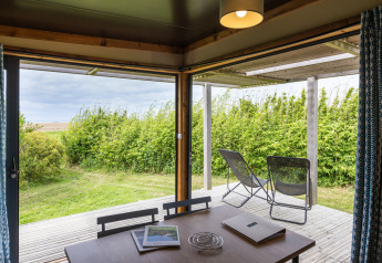 Blick aus Chalet Evasion Vista im Huttopia Les Falaises - Normandie auf die Terrasse mit grüner Landschaft.