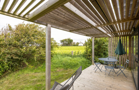 Houten terras met tuinmeubilair bij Chalet Evasion Vista, Huttopia Les Falaises - Normandie, uitkijkend over velden.