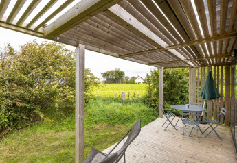 Holzterrasse mit Gartenmöbeln im Chalet Evasion Vista, Huttopia Les Falaises - Normandie, mit Blick auf Felder.