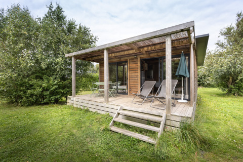 Cabaña de madera Chalet Ottawa con terraza techada, tumbonas y rodeada de vegetación.
