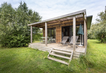 Træhytte Chalet Ottawa med overdækket terrasse og liggestole, omgivet af grønt og træer.