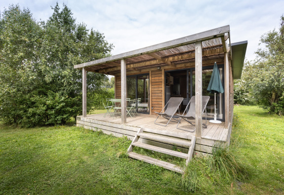 Cabaña de madera Chalet Ottawa con terraza techada, tumbonas y rodeada de vegetación.