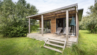 Cabaña de madera Chalet Ottawa con terraza techada, tumbonas y rodeada de vegetación.