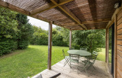 Terraza cubierta en Chalet Ottawa, Huttopia Les Falaises - Normandie, Francia, con mesa, sillas y jardín verde.