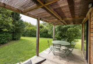 Terraza cubierta en Chalet Ottawa, Huttopia Les Falaises - Normandie, Francia, con mesa, sillas y jardín verde.